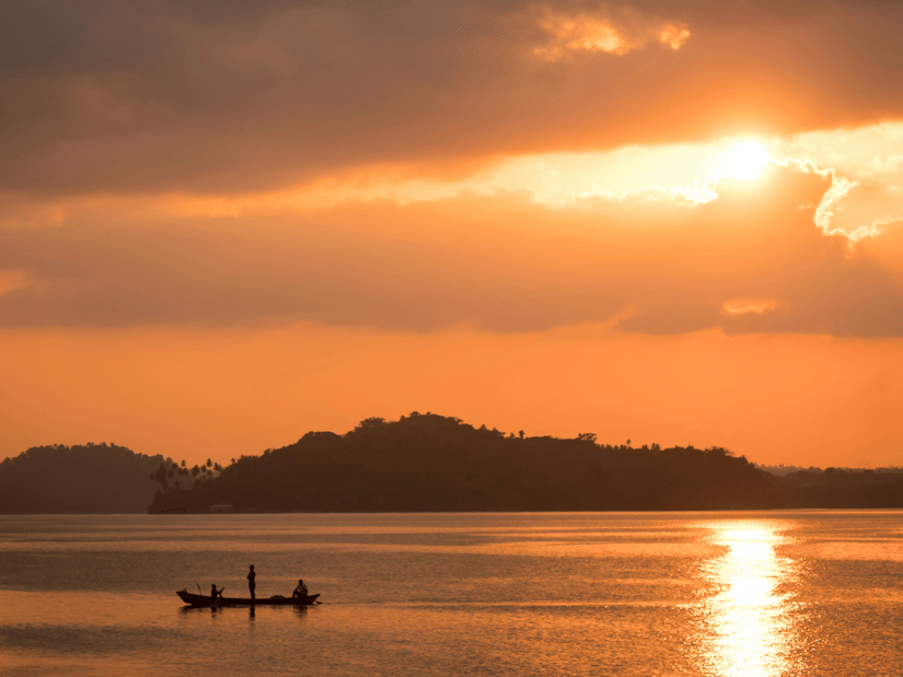 A beach near Havelock Island with the sun setting in the background and a boat travelling on the waterbody.