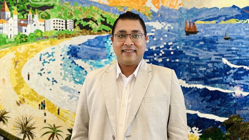 A person wearing a light-colored suit stands in front of a brightly colored, abstract painting.