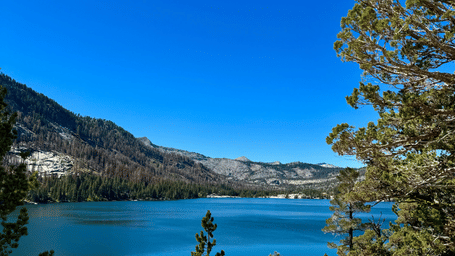 A wide-angle shot of a lake with a deep blue hue under a clear sky surrounded by mountain ranges.