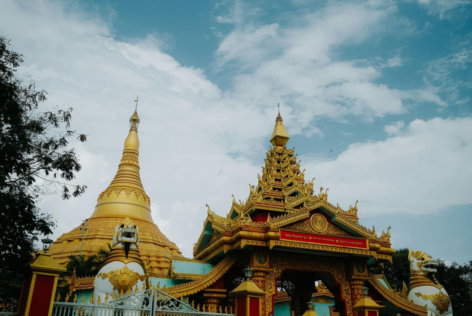A vibrant golden temple with intricate carvings and a large gate, set against a bright blue sky with white clouds.