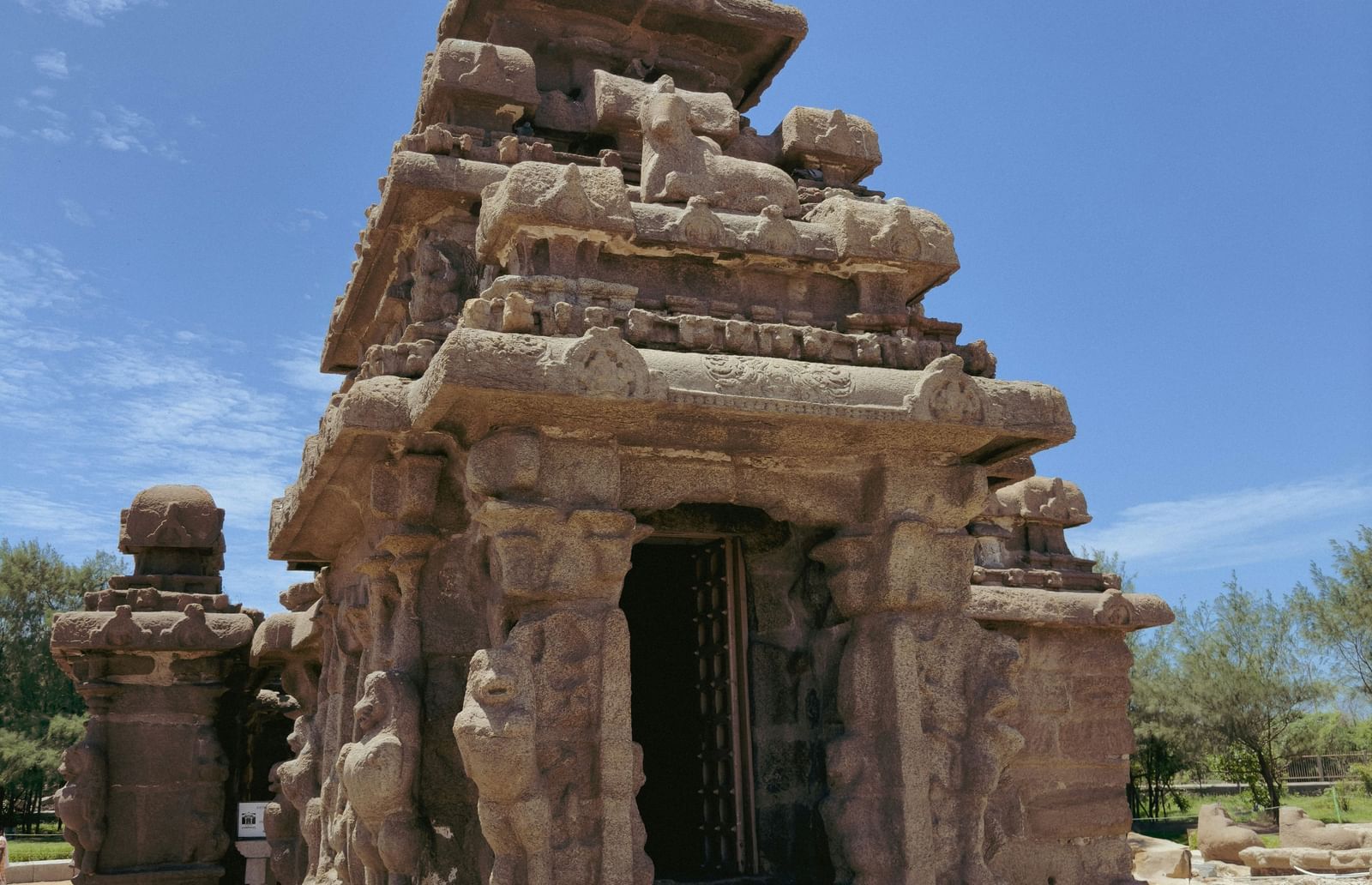 A vertical shot of a multi-tiered, carved stone temple with a bell-shaped top, set against a bright blue sky.