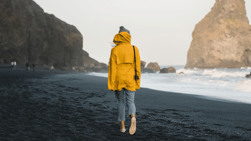 a person walking on a black sandy beach with a mountain in the background