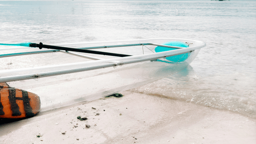 a transparent boat parked in white sandy beach with clouds on blue sky in the background