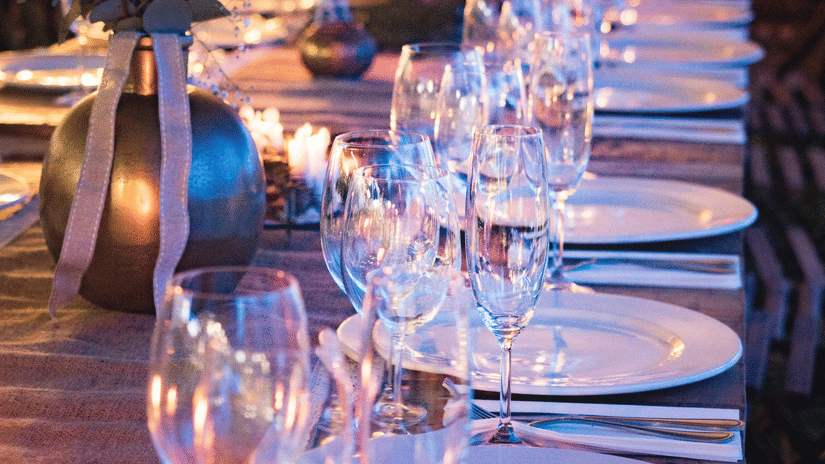 Banquet table set with plates, wine glasses, candles and floral centrepieces for an evening event.