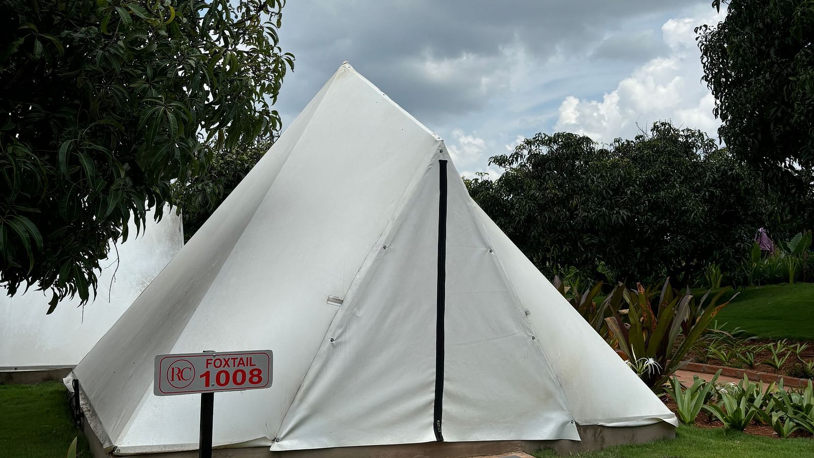 A scenic view of a resort area with tents lined along a neat walkway, surrounded by a well-maintained lawn.
