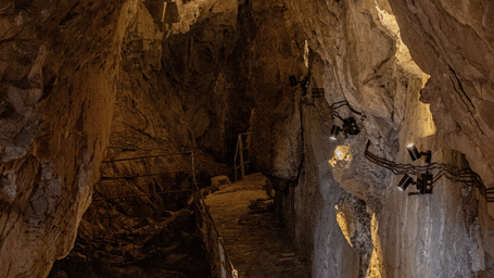 Narrow stone passage inside a naturally formed cave shrine illuminated with warm lighting.