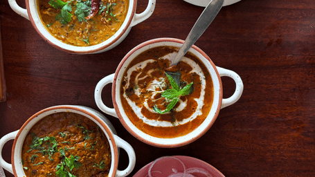 Flat lay of traditional Indian cuisine featuring several curries in bowls and a side plate of sliced onions.