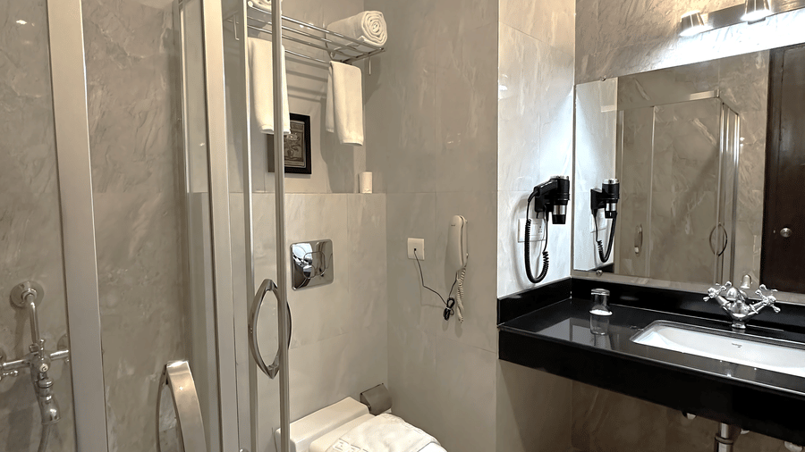 Modern bathroom in the Superior Room at A S Hotels, Khajuraho, featuring a glass shower cubicle, marble tiling, and a sleek vanity with a large mirror.