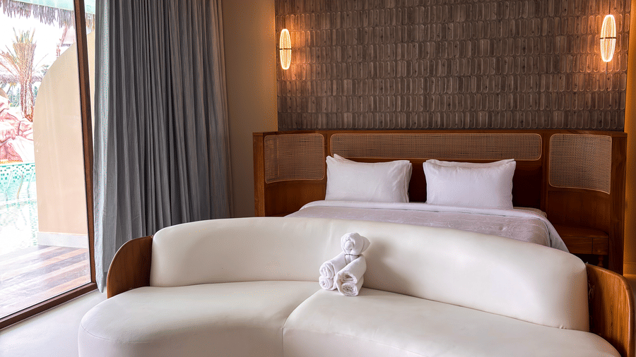 A large bed with a textured headboard sits behind a curved white sofa and a ceiling fan in a room at Avanya Resorts N Retreat.