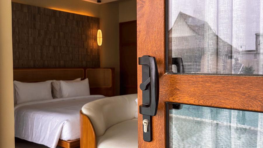 A wooden door with a black handle is partially open, revealing a white curved sofa and a bed inside a room at Avanya Resorts N Retreat.
