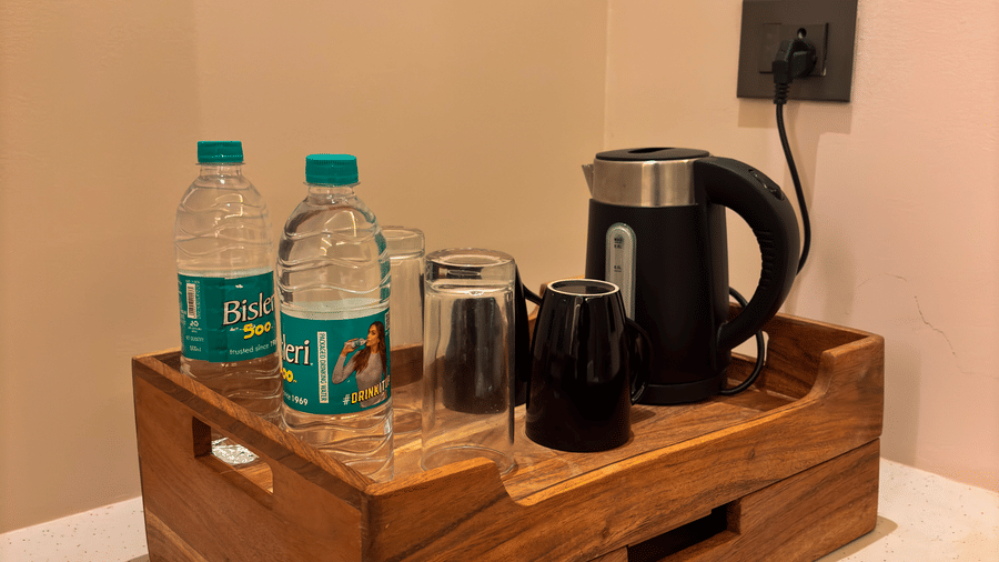 A wooden tray holds 2 bottles of water, a black electric kettle, and 2 black mugs on a white counter at Avanya Resorts N Retreat.