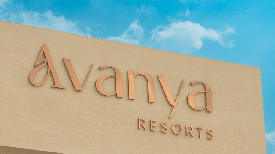 The 'Avanya Resorts' name is displayed in gold lettering on a beige exterior wall against a clear blue sky at Avanya Resorts N Retreat.