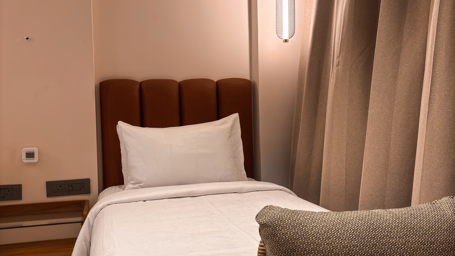 A single bed with a brown headboard, white pillows, and a grey armchair in the foreground at Avanya Resorts N Retreat.