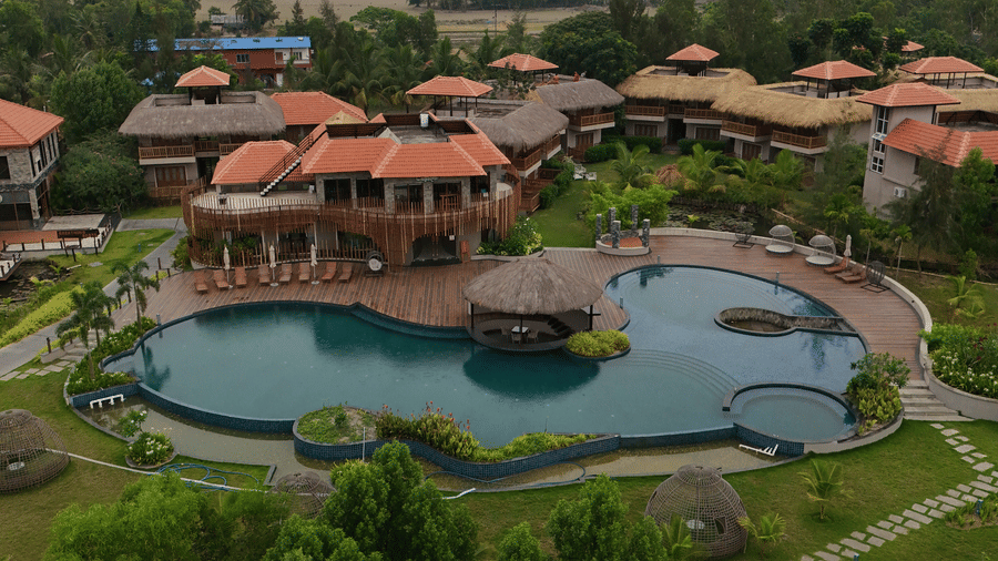 Aerial view of Hotel Sonar Bangla, Sundarban featuring an outdoor swimming pool and multiple brown-roofed buildings.