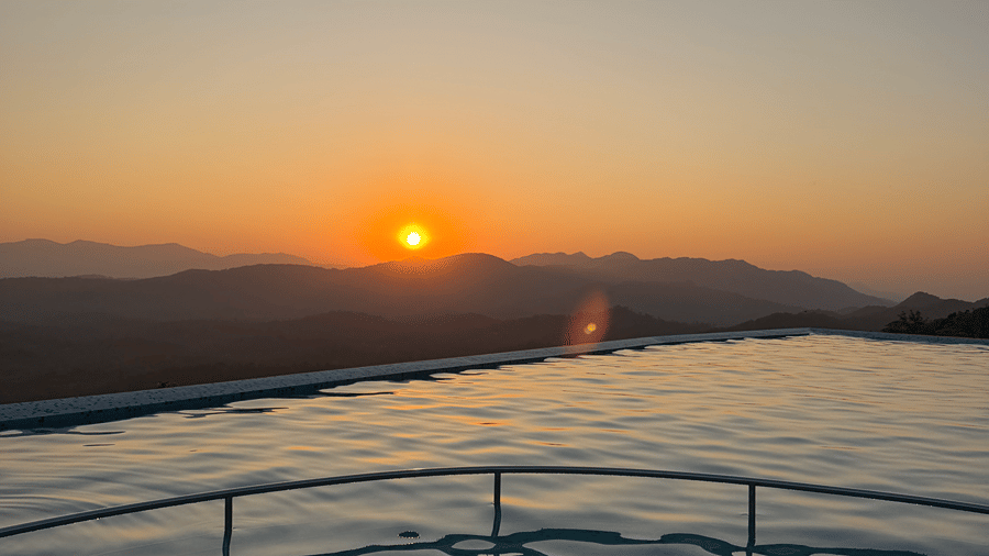A sunset over distant hills viewed from the edge of an infinity pool | Kollanoor Guest House, Coorg