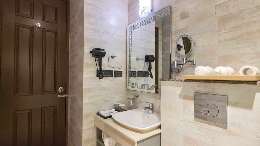 Side view of a bathroom featuring a a well stocked vanity area with a wash basin and a mirror above it beside a commode at The Meriton.