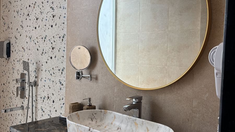 Modern bathroom with black counter, round mirror, and wall-mounted light at Tisya Farms, Gurgaon.