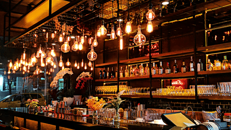 Warm pendant lights illuminate a stylishly designed counter with bar stools at a modern lounge.