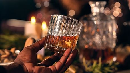 An overview of a person holding a glass of whisky while another person is looking in the background.