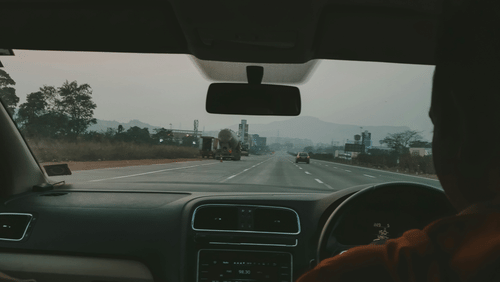 A silhouette of a person behind the steering wheel of a car driving on a highway.