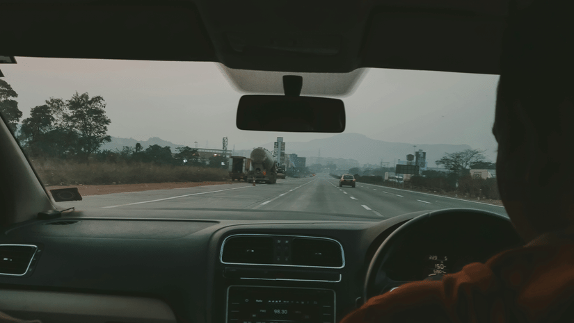 A silhouette of a person behind the steering wheel of a car driving on a highway.
