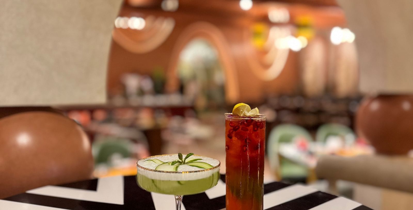 A close-up of a cocktail drink on a black and white patterned table at Themis Barbecue House, Ambala, with a blurred background.