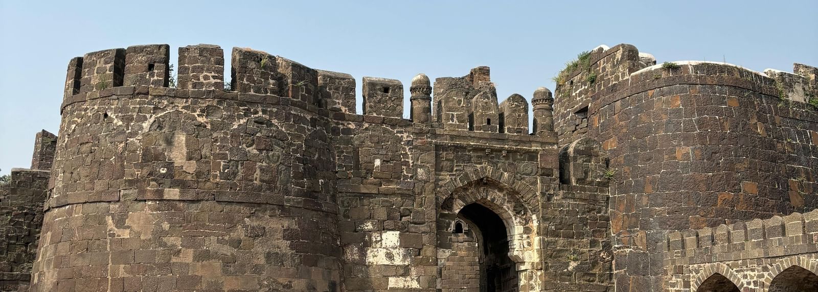 Entrance of an ancient stone fort with high walls and an arched gateway.