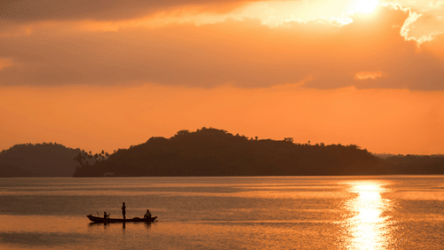 A beach near Havelock Island with the sun setting in the background and a boat travelling on the waterbody.