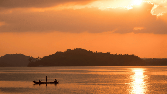 A beach near Havelock Island with the sun setting in the background and a boat travelling on the waterbody.
