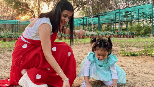A woman holding a swing watching a young girl play in the sand in outdoors - Karma Lakelands.