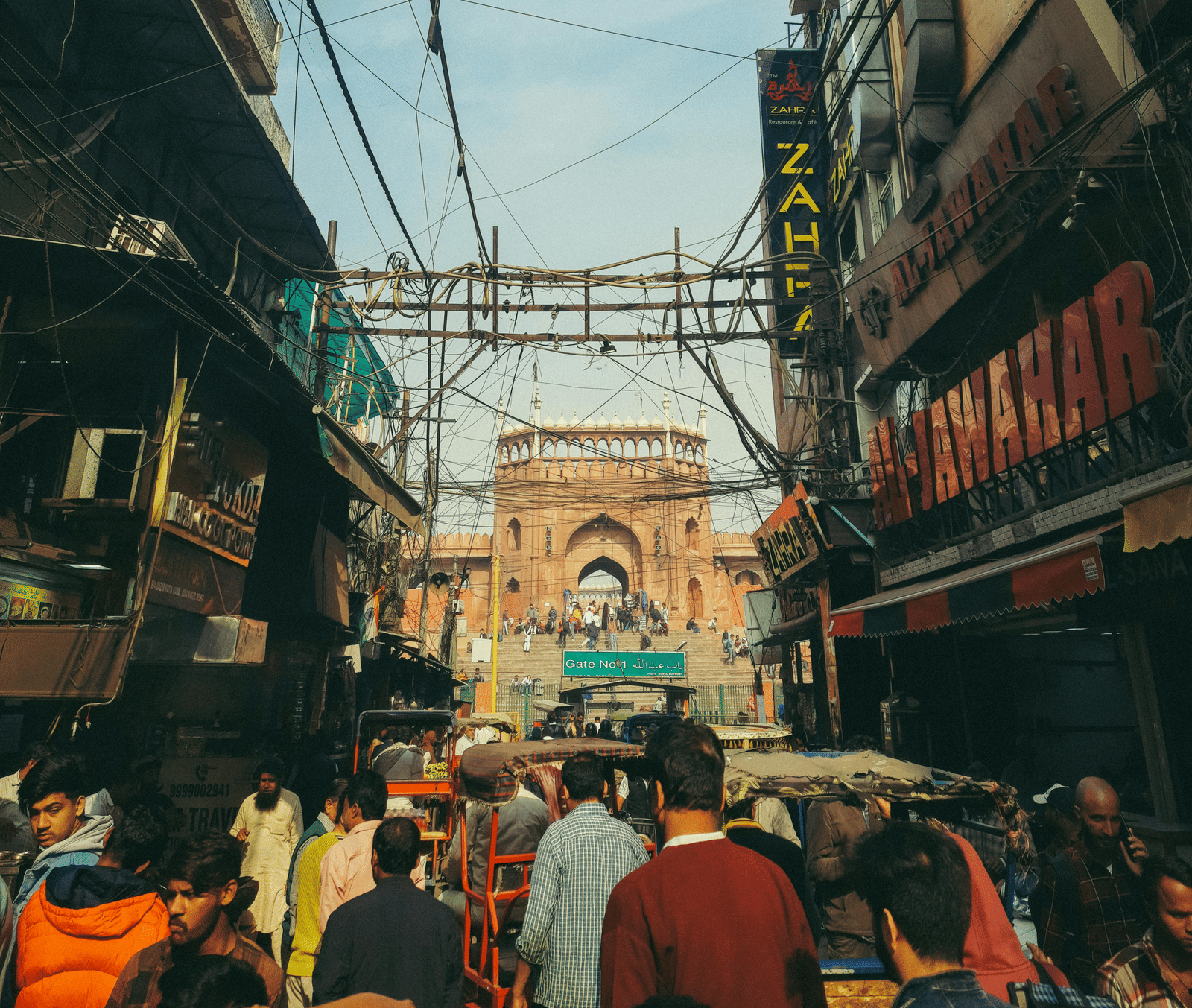 Busy street market scene in India with people, buildings, and overhead wires.