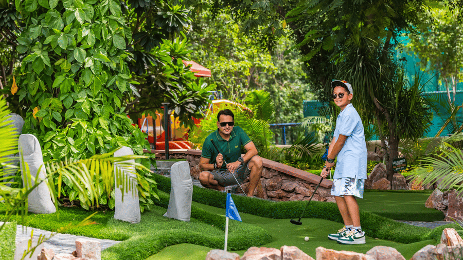 A man and a child at a mini golf range at the Heritage Village Resort & Spa, Manesar, with one holding the golf  club.