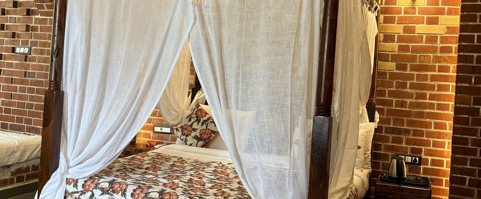 Bedroom with a four-poster canopy bed, brick wall accents, and warm lighting at Tisya Farms, Gurgaon.