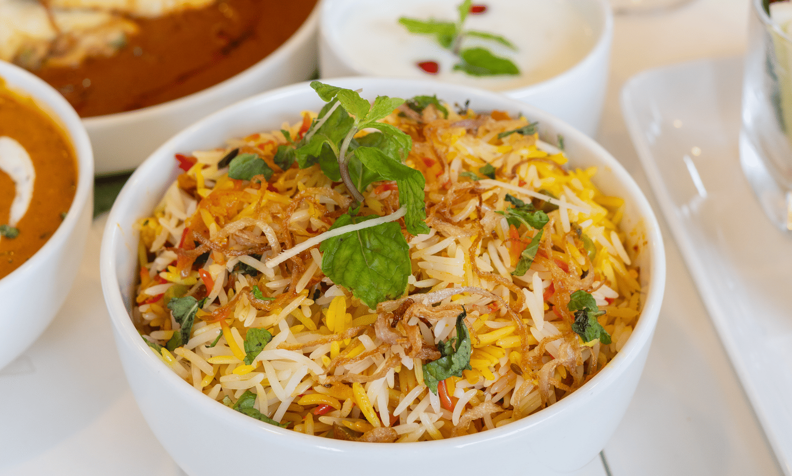 A table setting featuring a large portion of biryani in a white bowl with side dishes - Megha Resort & Villas, Dehradun