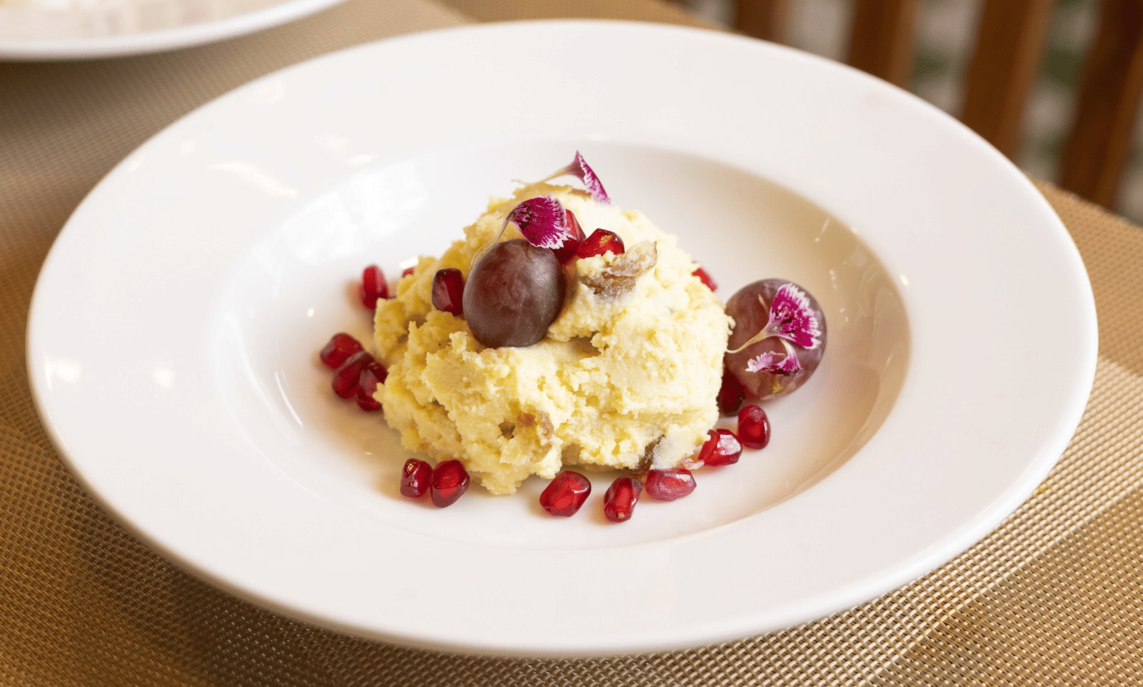 A white plate holds a small portion of a gourmet main course garnished with pomegranate seeds - Megha Resort & Villas, Dehradun