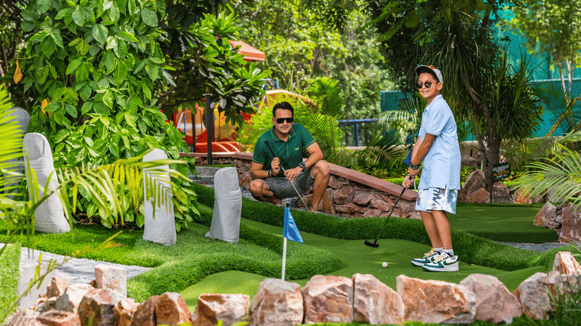 A man and a child at a mini golf range at the Heritage Village Resort & Spa, Manesar, with one holding the golf  club.