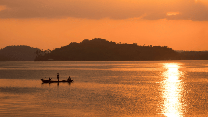 An overview of a beach near Havelock Island with the sun setting in the background and a boat travelling on the waterbody.
