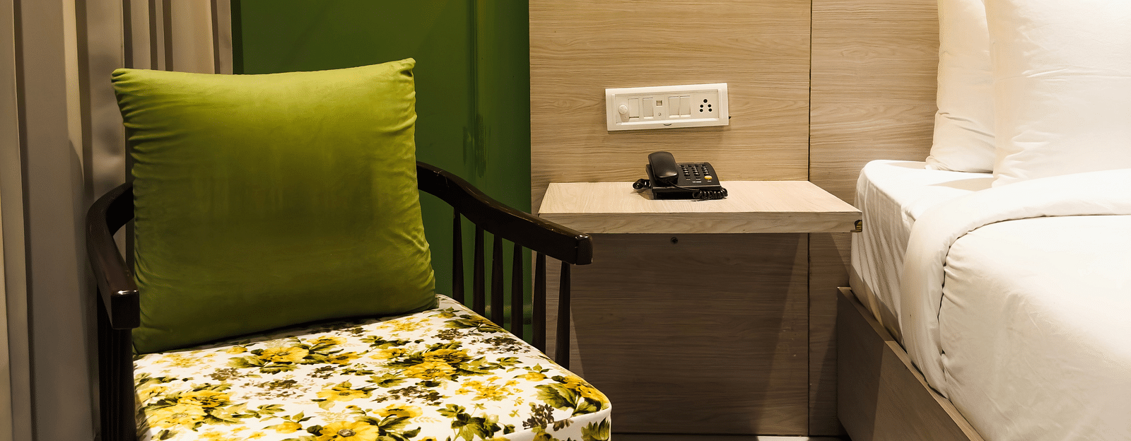 A view of a green sofa with a patterned cushion near a bed in the deluxe room - Wonder Hills