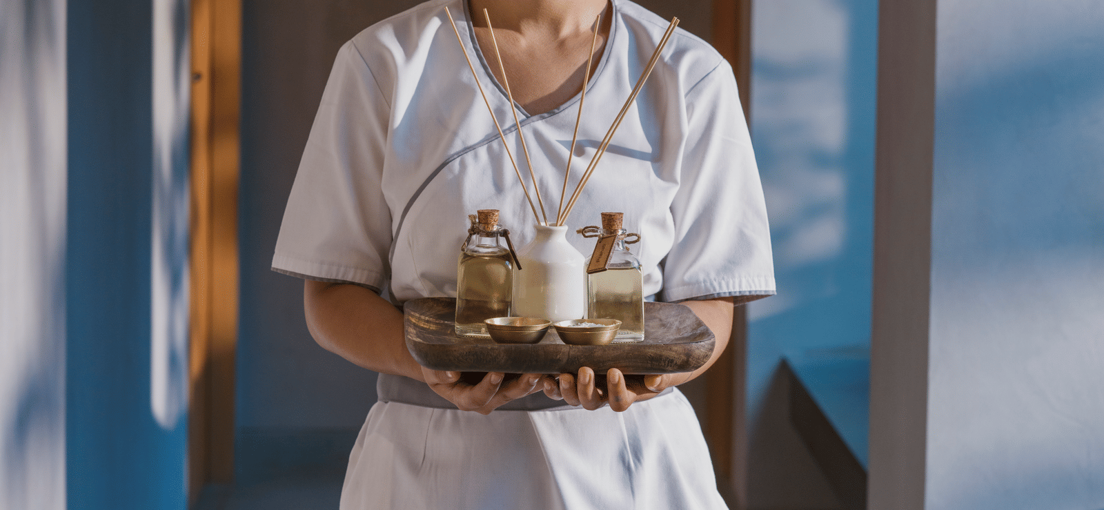 A portrait shot of a staff member at Athiva Hotels holding a wooden tray with vials of essential oils | Resorts in Khandala for couples