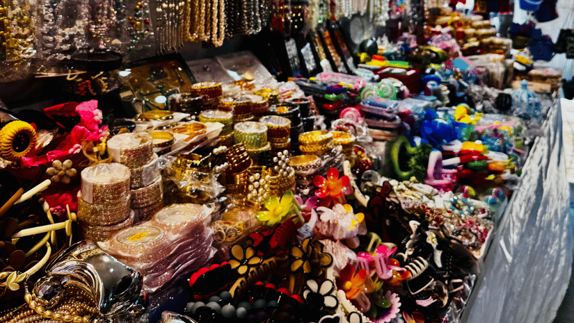 A vibrant market stall overflowing with colourful beaded necklaces, bracelets, and traditional ornaments displayed under bright lights.