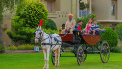A family seated in a decorated horse-drawn carriage on the resort lawn at Heritage Village Resorts & Spa, Manesar.
