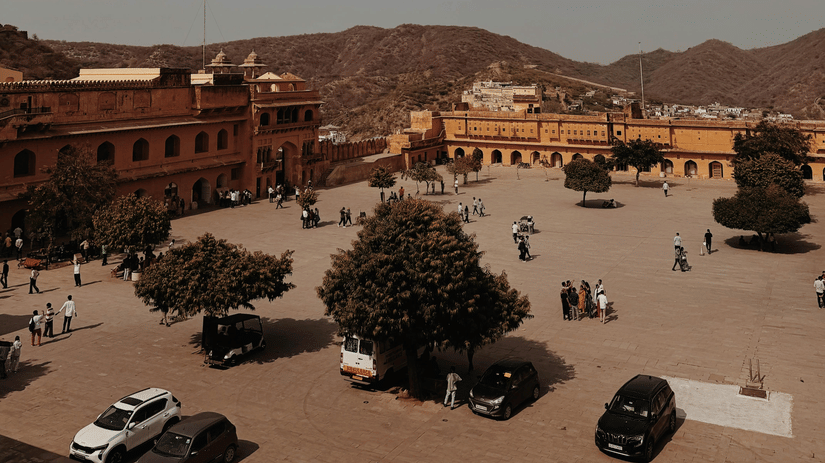 A wide internal courtyard of a sandstone fort, with several parked cars and people walking about.