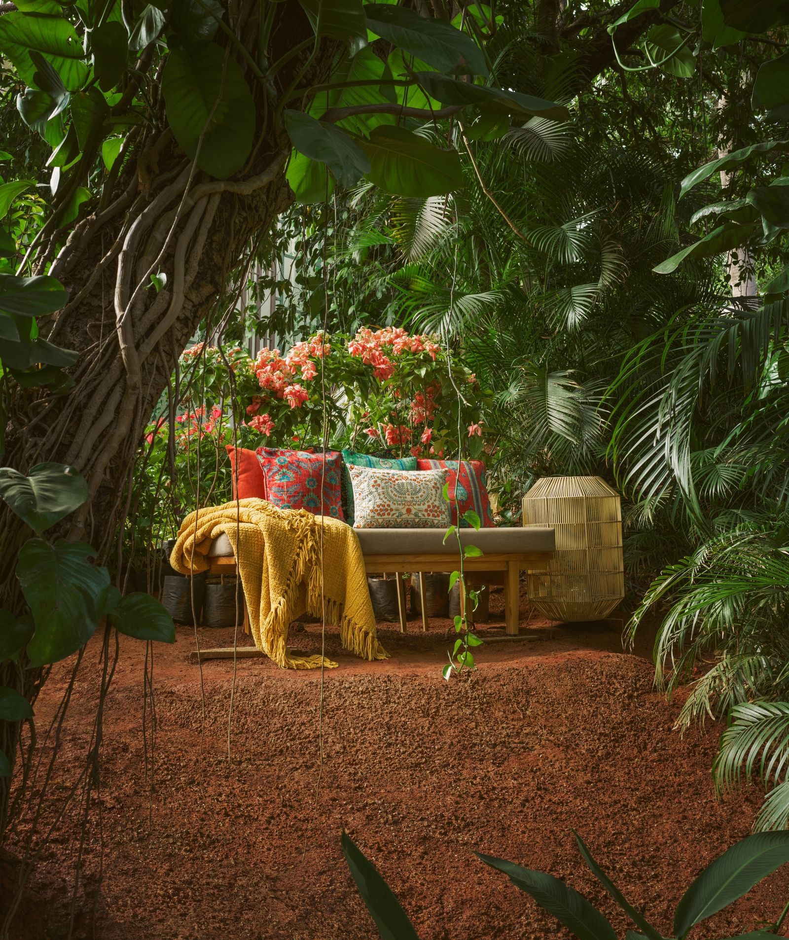 A wooden daybed with colourful pillows and a yellow throw blanket, set in a lush tropical garden surrounded by dense green foliage at Athiva Hotels | Best season to visit Lonavala