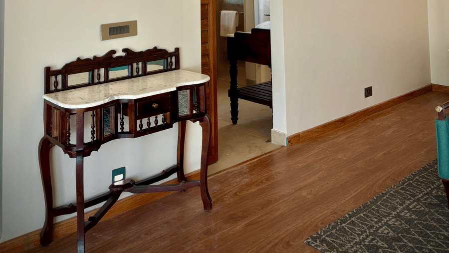 Interior of the Vana Suite featuring a table with drawers, a lamp, and an air conditioner at Surpura Bagh.