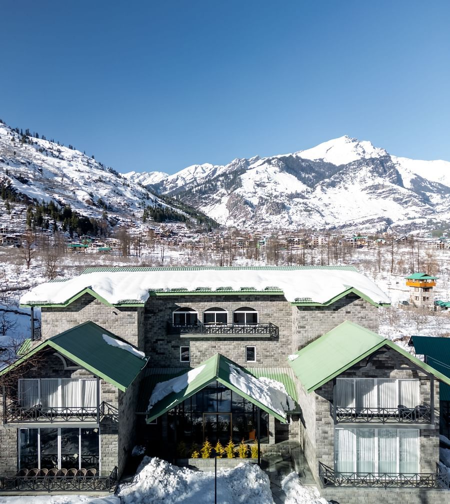 Scenic view of snow-capped mountains behind Nivasana Manali in daylight.