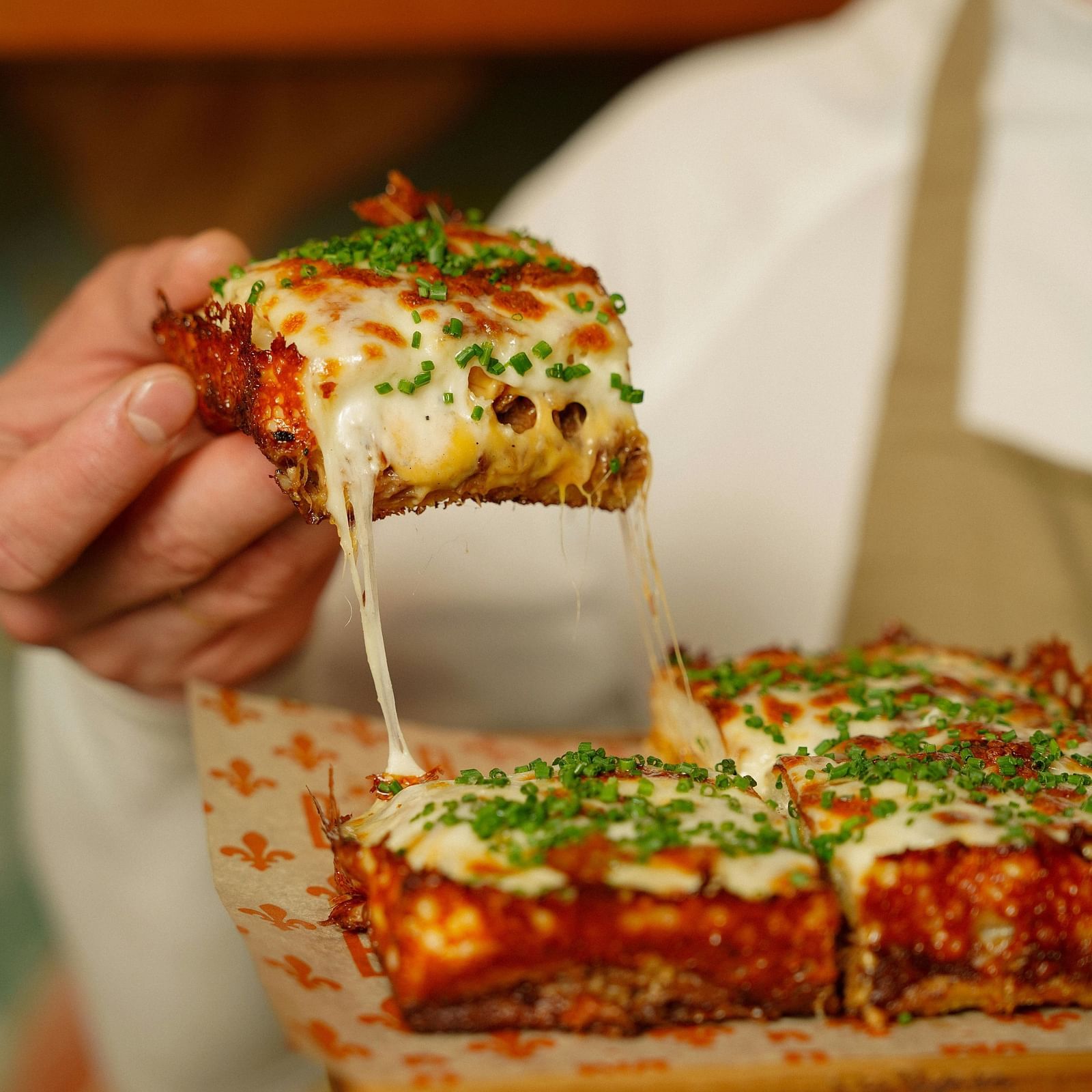 A chef presenting a cheesy slice of lasagne garnished with chives