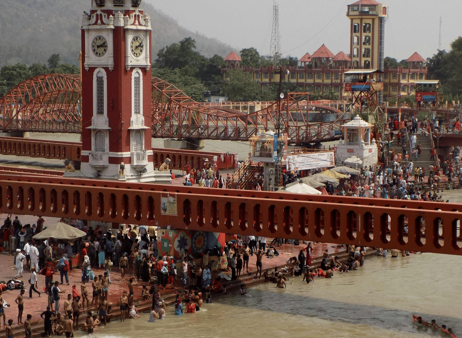 Huge crowds of devotees gathered on the banks of a river with a bridge going over the river.