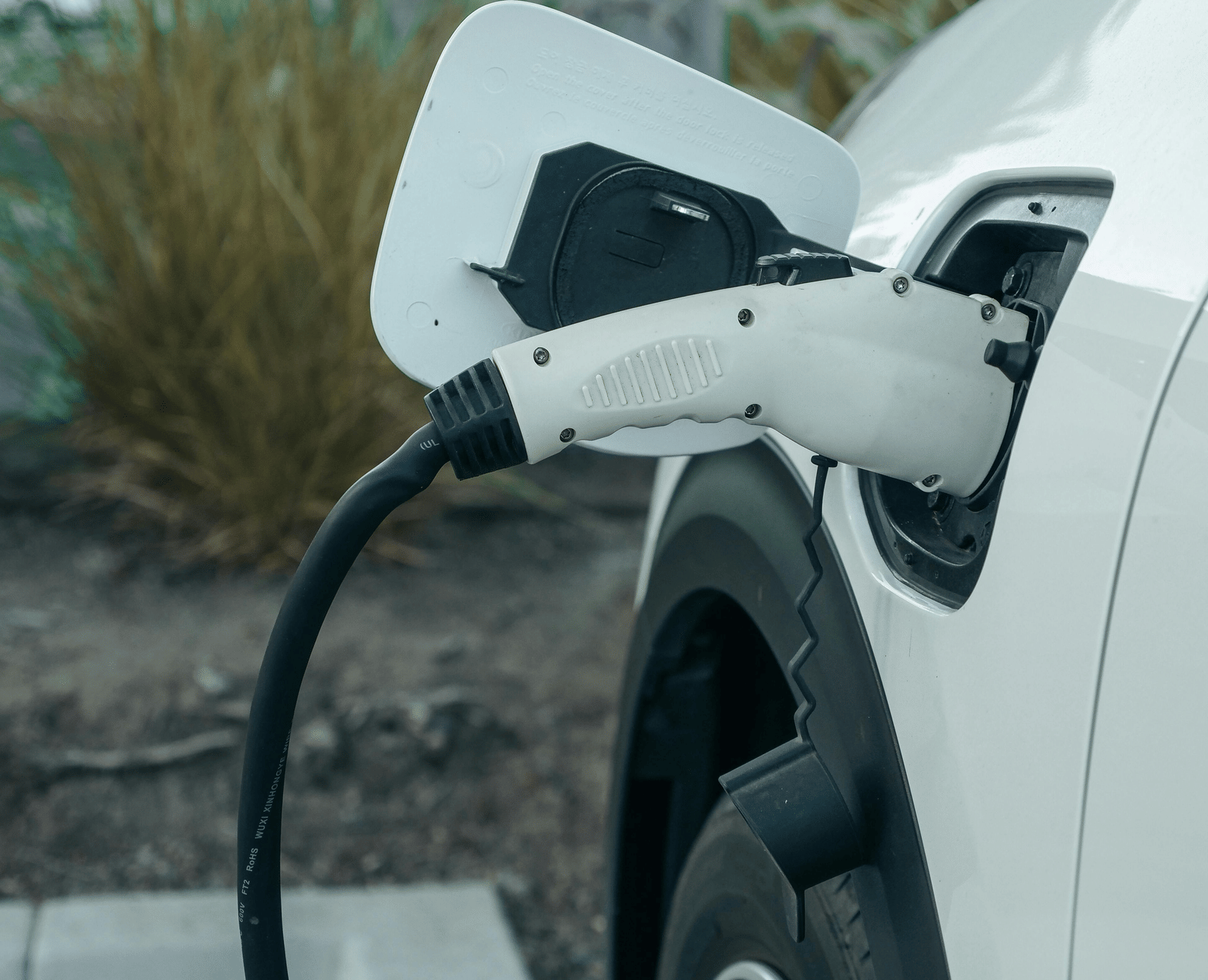 A white electric vehicle parked with a charging cable plugged into its charging port.