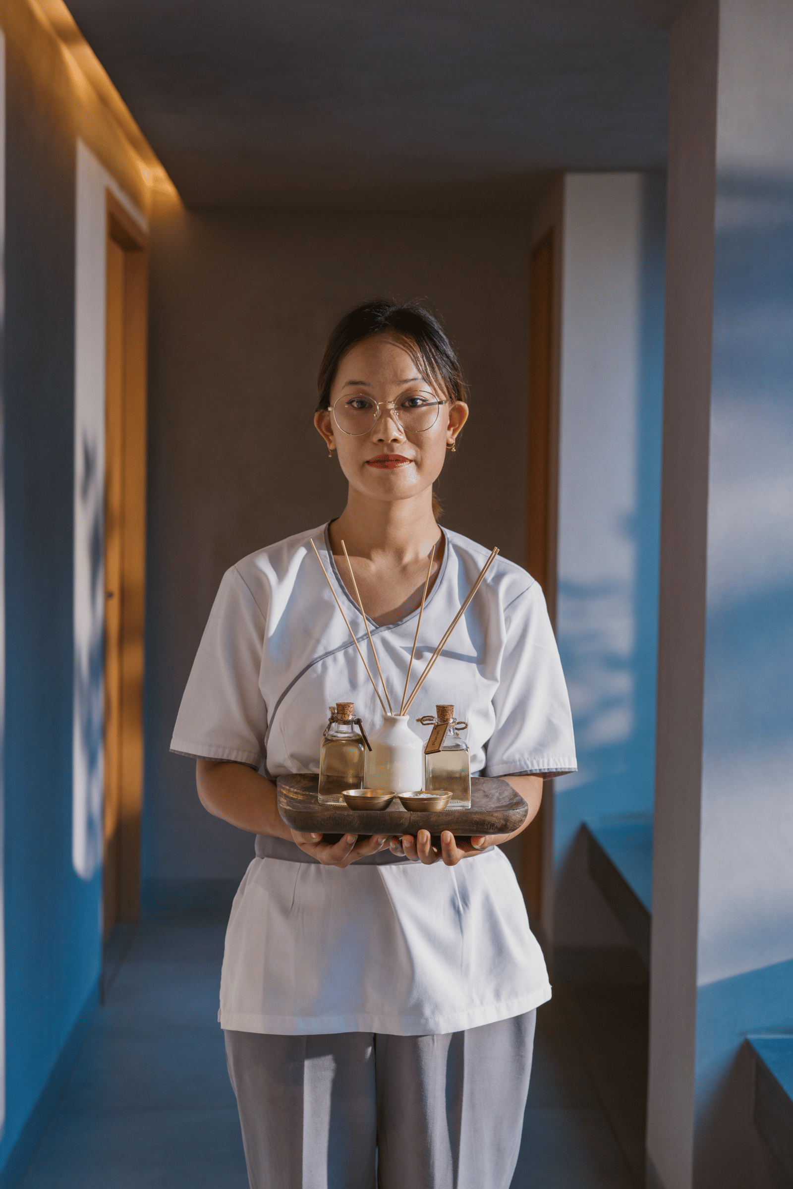 A portrait shot of a staff member at Athiva Hotels holding a wooden tray with vials of essential oils | Resorts in Khandala for couples