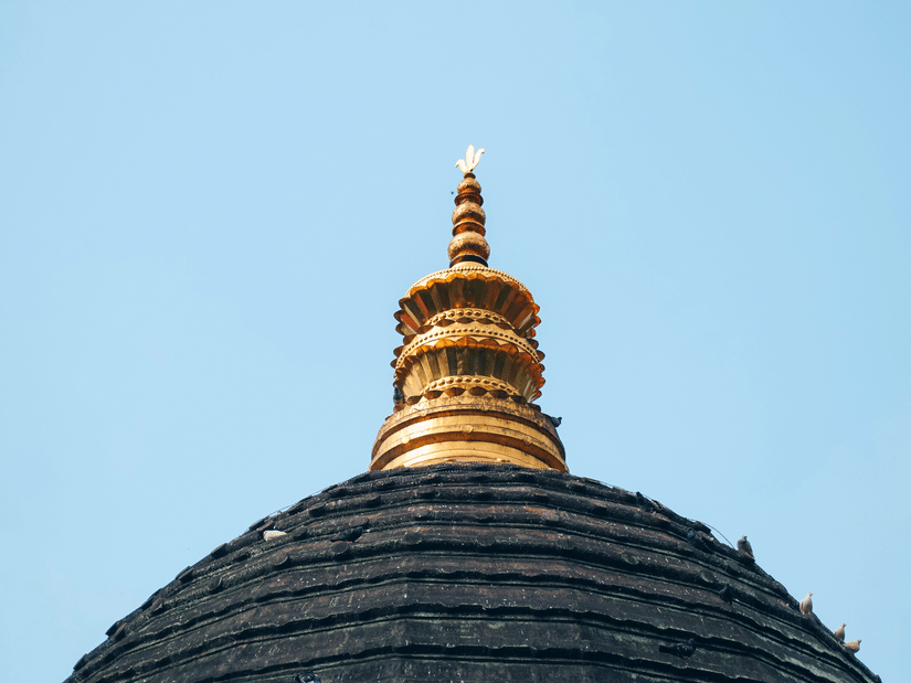 A domed temple roof topped with a gleaming golden finial against a pale sky